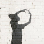 Young woman forming a heart with her hands around on the brick wall background. Photo of shadows of girl